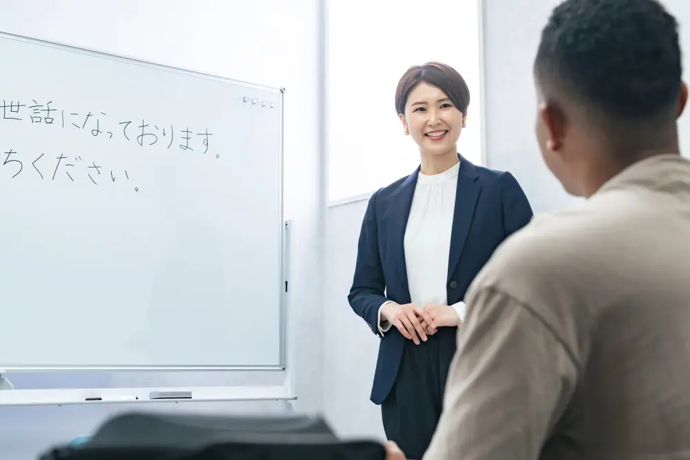 日本語を学ぶ外国人向けの授業風景です。講師がホワイトボードで説明しています。